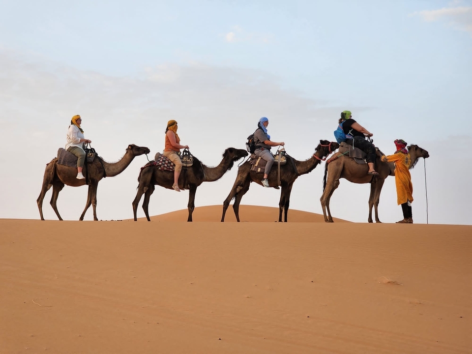 People riding camels in the desert at sunset.