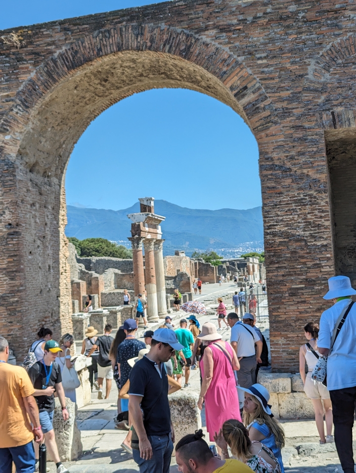 Ancient city ruins with tourists and mountains in the background.