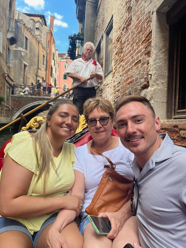 People in a gondola on a canal with other tourists in the background.