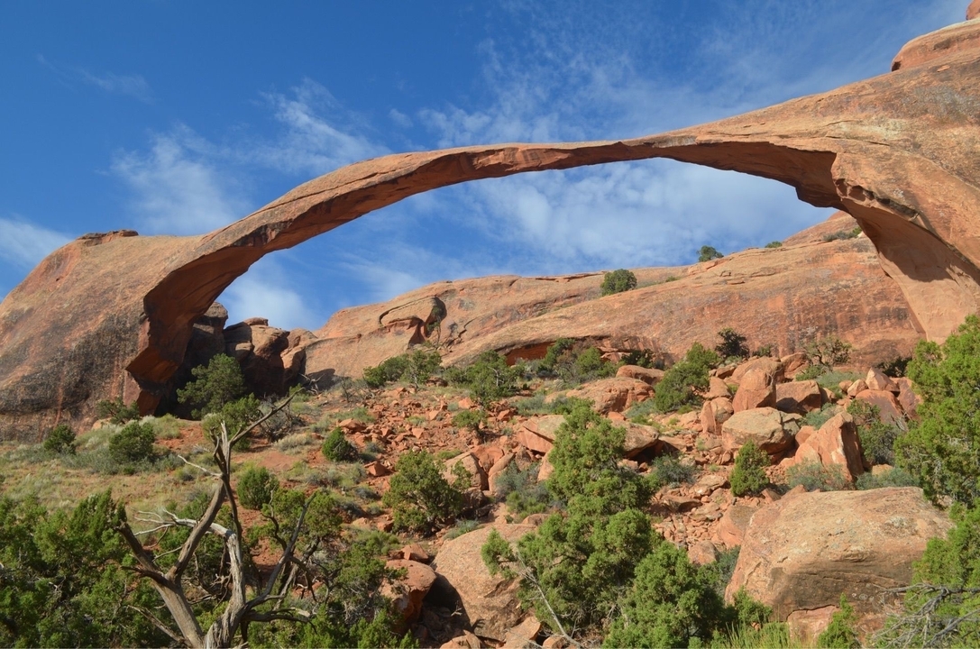 Une arche de pierre naturelle dans un paysage désertique sous un ciel bleu.
