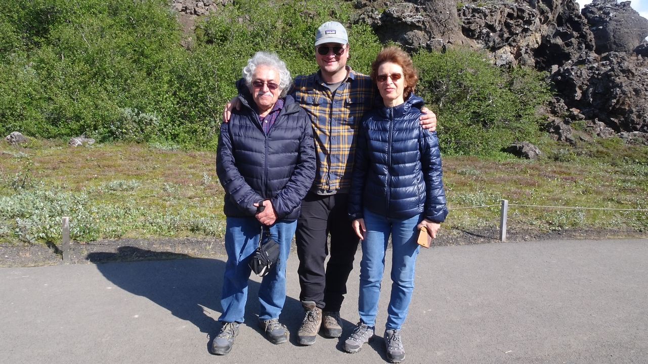 A group of three people in outdoor clothing standing on a gravel path.