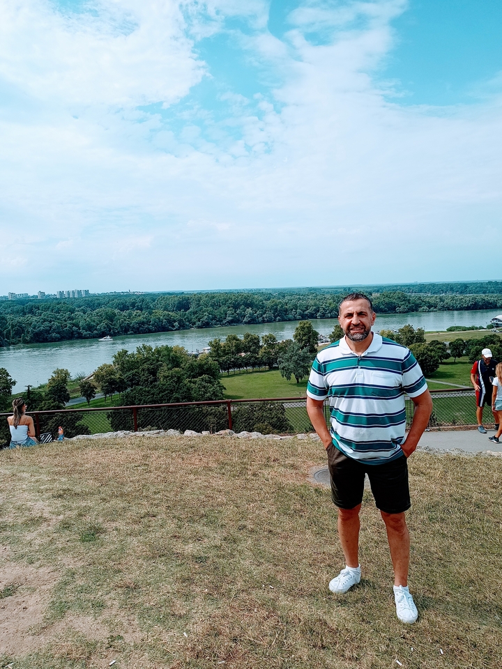 A man posing near a river with a scenic background.