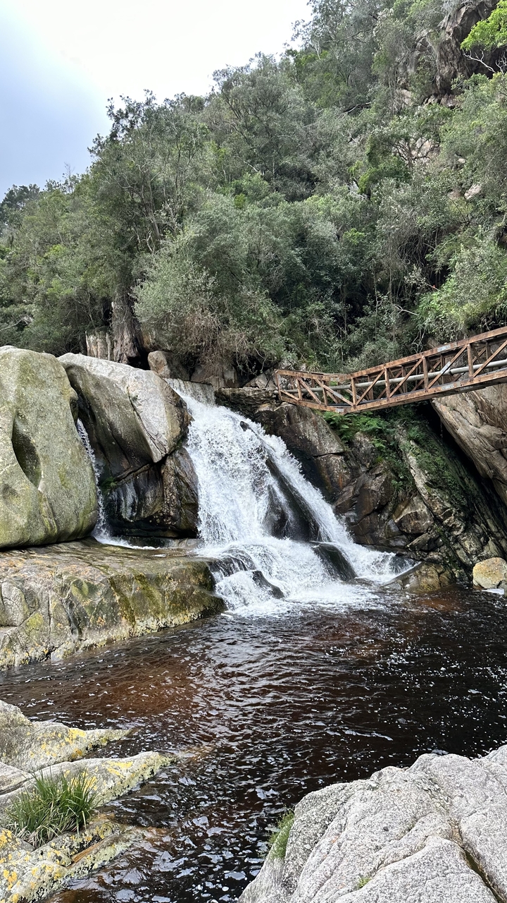 A waterfall with rocks and a metal bridge above.