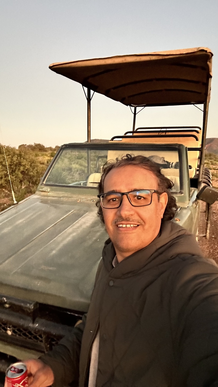 A person taking a selfie with a safari vehicle in a natural setting.