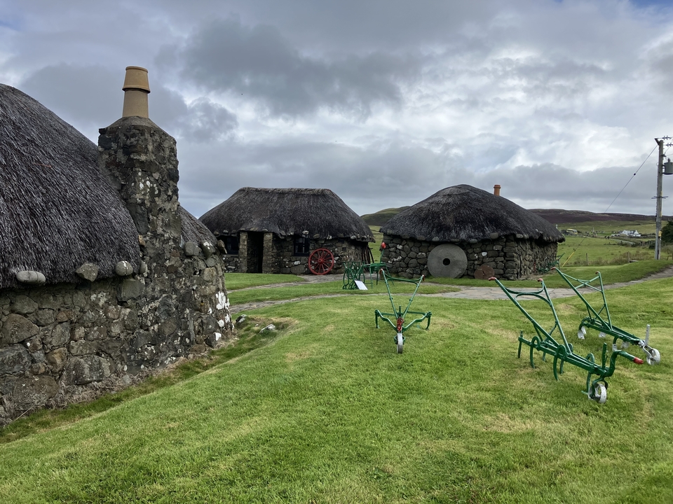 Thatched stone houses with green machinery and a wheel.