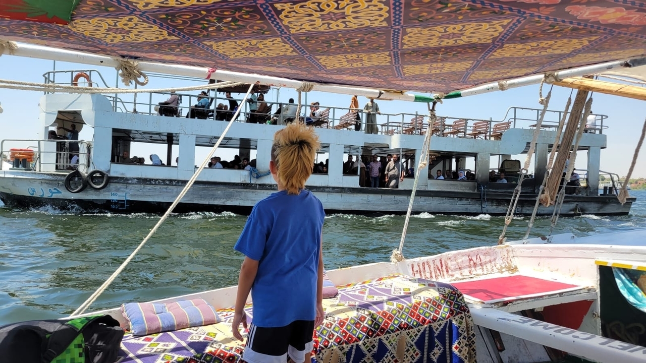Boy on a sailboat looking at another boat on the water.