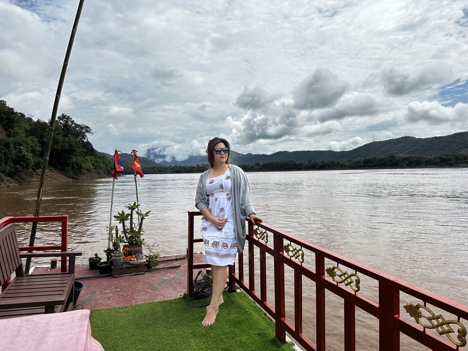 Femme posant sur un bateau avec une rivière et des montagnes en arrière-plan.