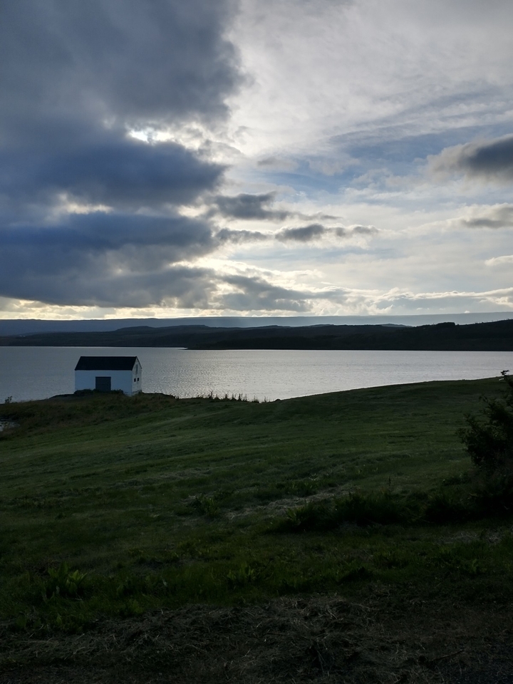 Lone house by a serene lake with cloudy sky.