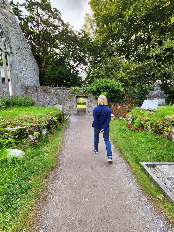 Person walking through a stone archway surrounded by greenery.