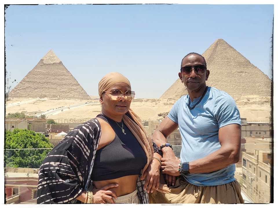 Two people posing in front of pyramids under a clear sky, photo has a frame effect.