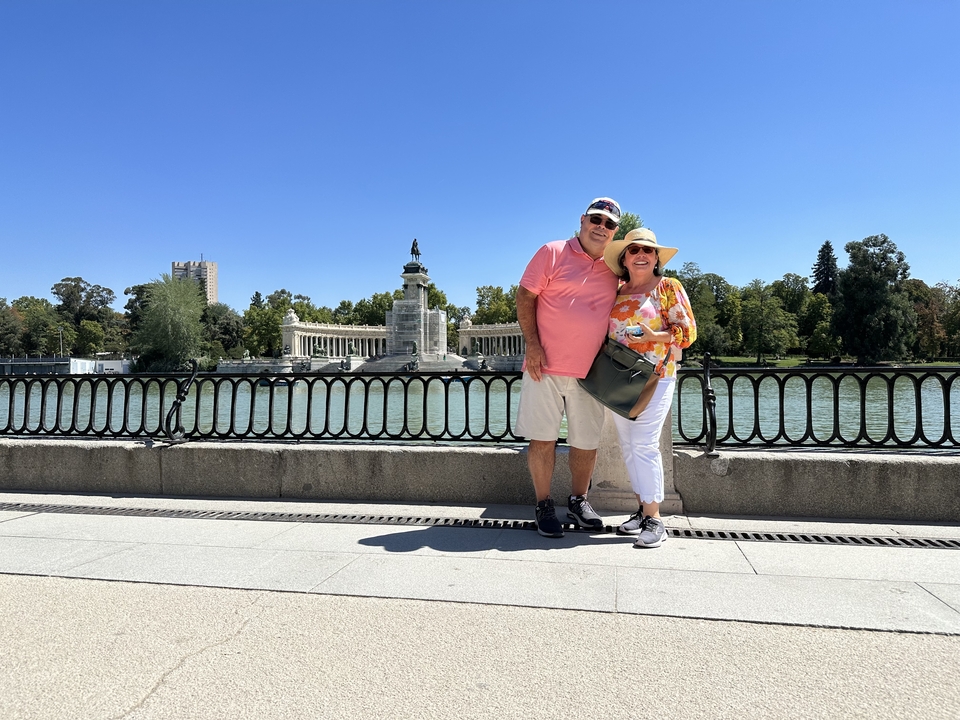 Couple posing by a lake with a stone monument behind.