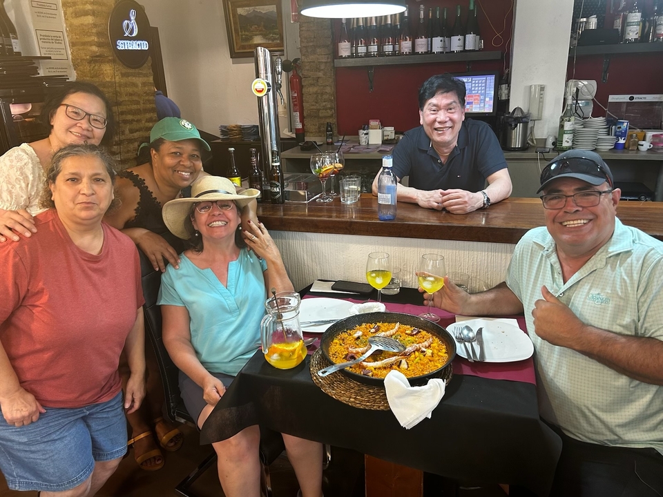 A group of people smiling around a table with a paella dish.