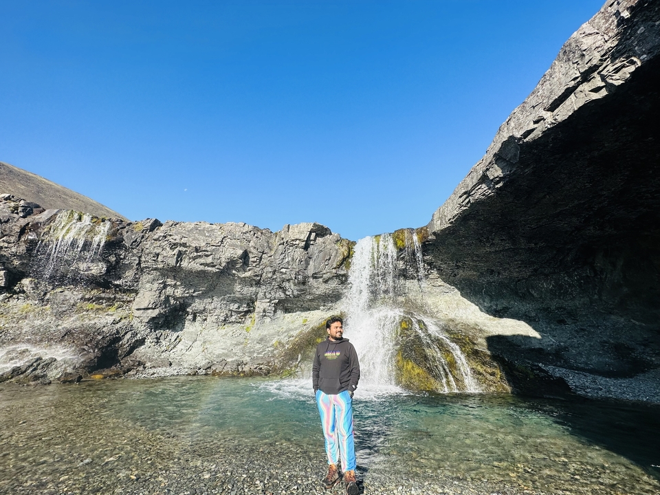 A person standing in front of a waterfall with blue sky in the background.