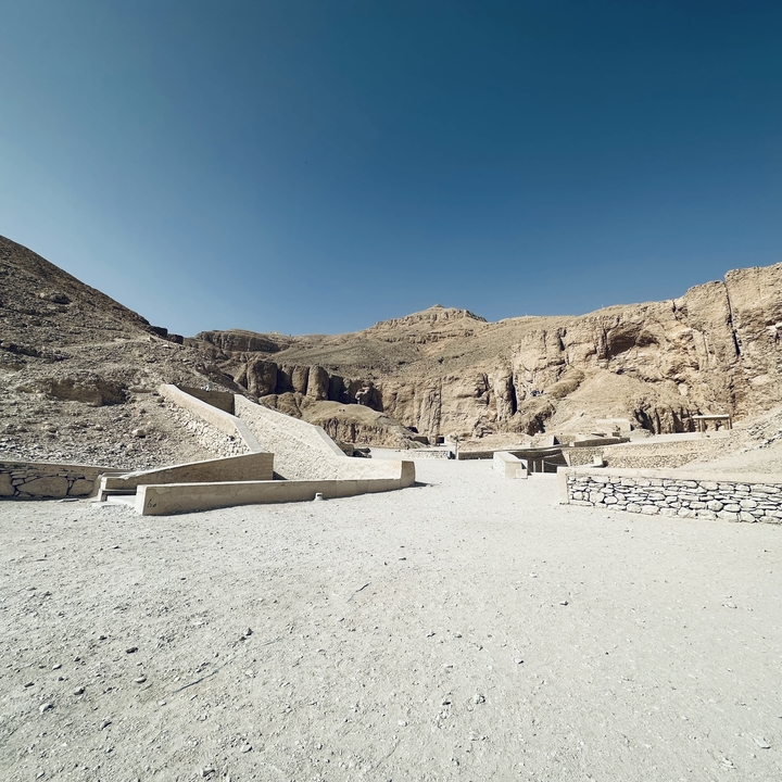 Vallée désertique ouverte avec des ruines antiques et des sentiers de sable.