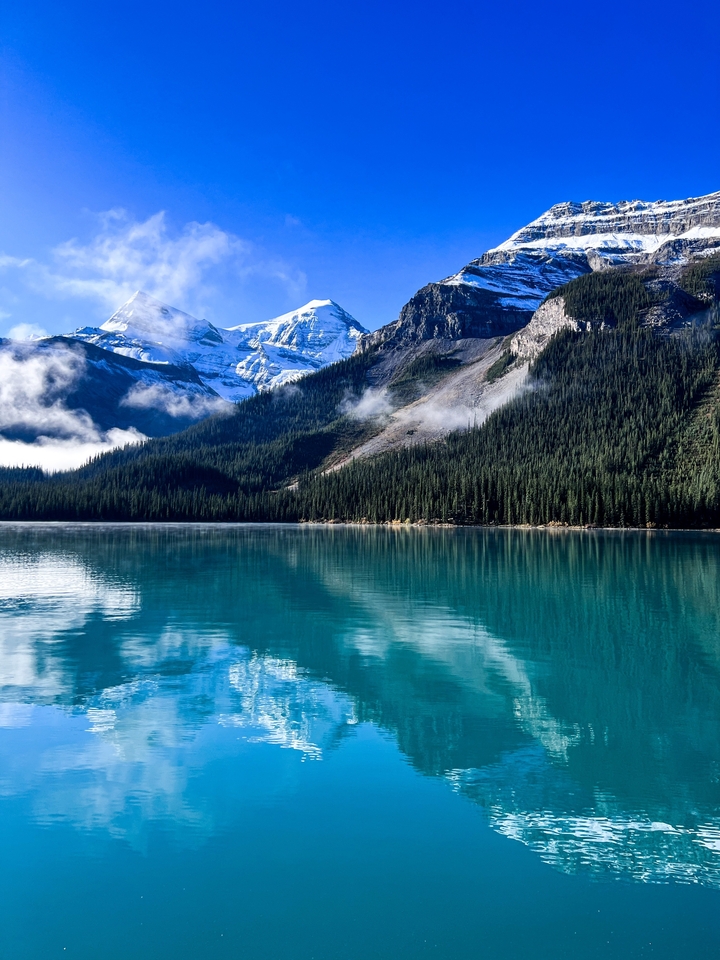Lac pristine entouré d'une forêt dense et de montagnes.