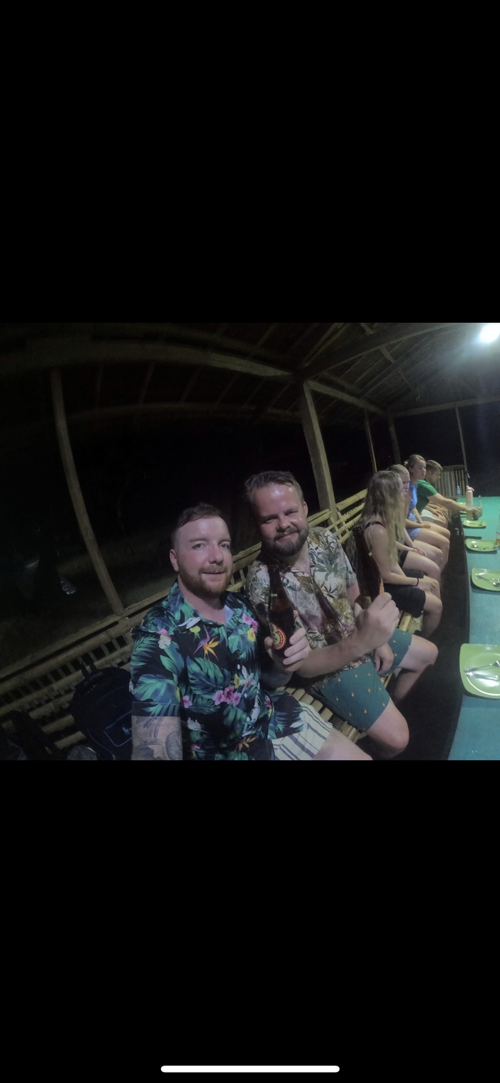 Des gens assis à une table à l'extérieur la nuit, tenant des bouteilles.