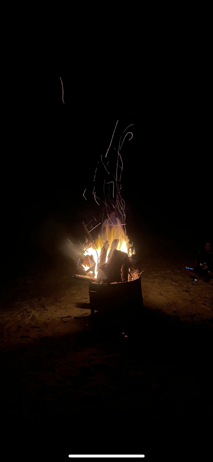 Feu de camp qui brûle la nuit sur une plage.