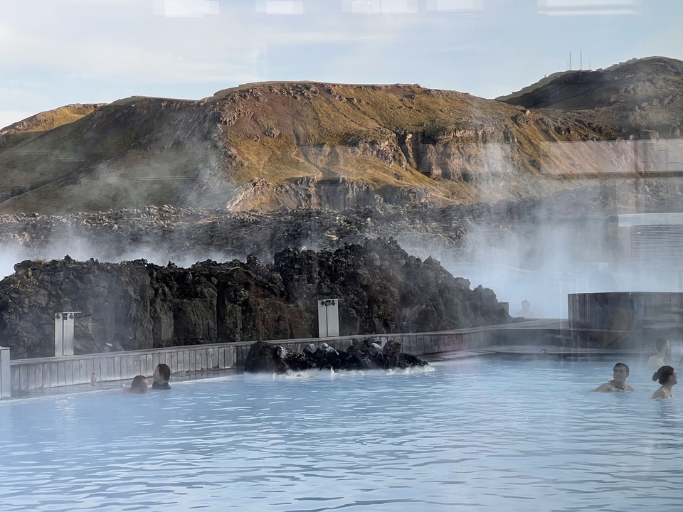 People in a steaming geothermal pool with rocky landscape.