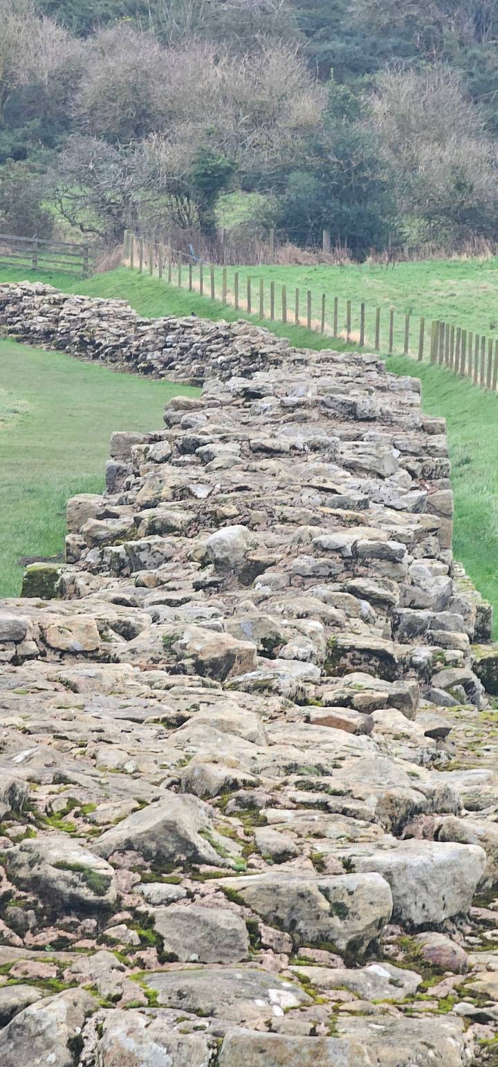 A stone wall extending along a grassy field.