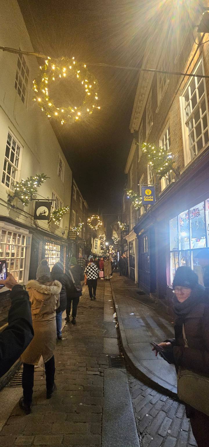 A busy street at night with people walking and festive decorations overhead.