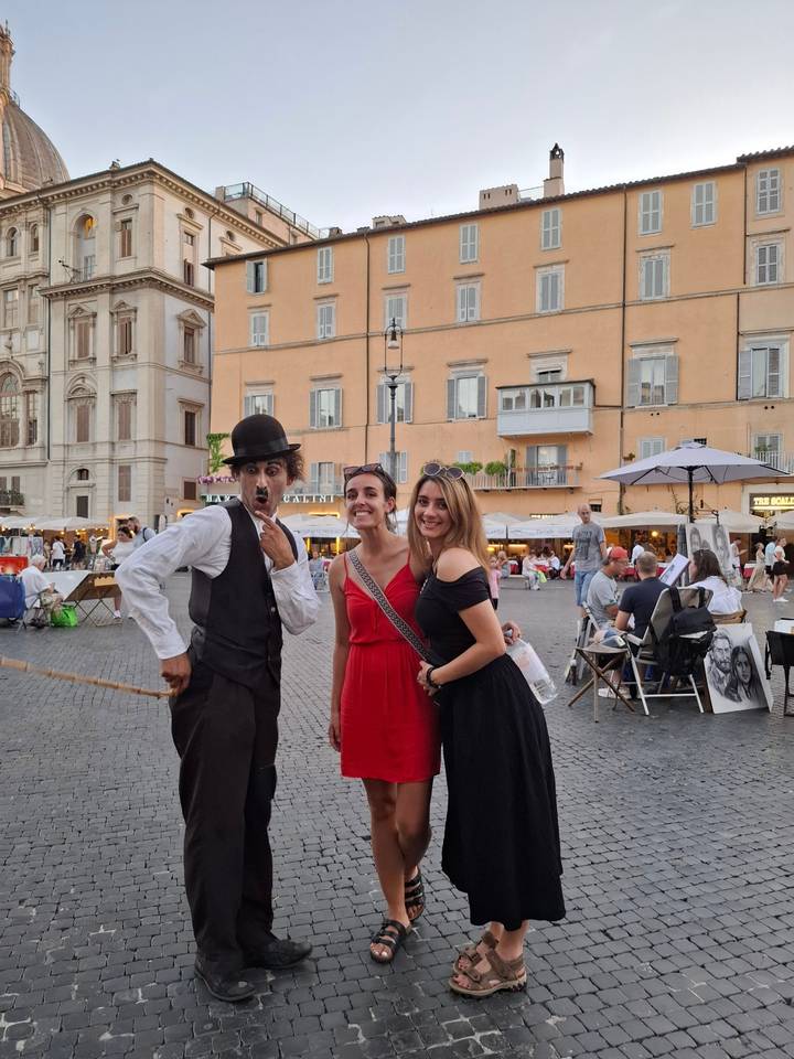 Three people posing in a city square with shops.