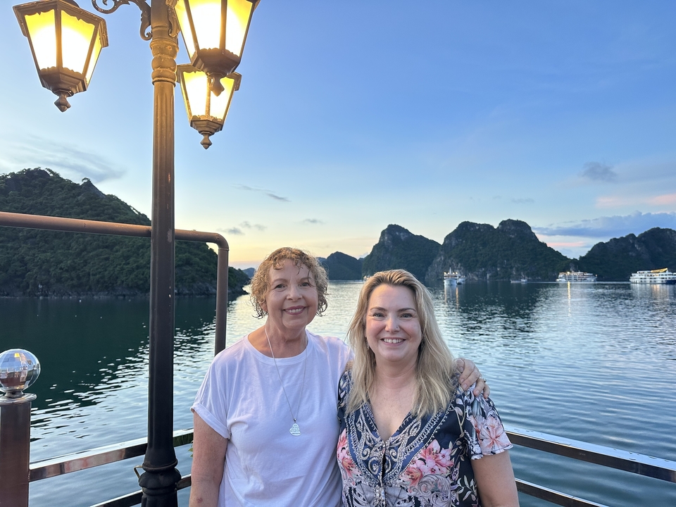 Deux femmes posant joyeusement avec une vue panoramique sur les montagnes et l'eau en arrière-plan.