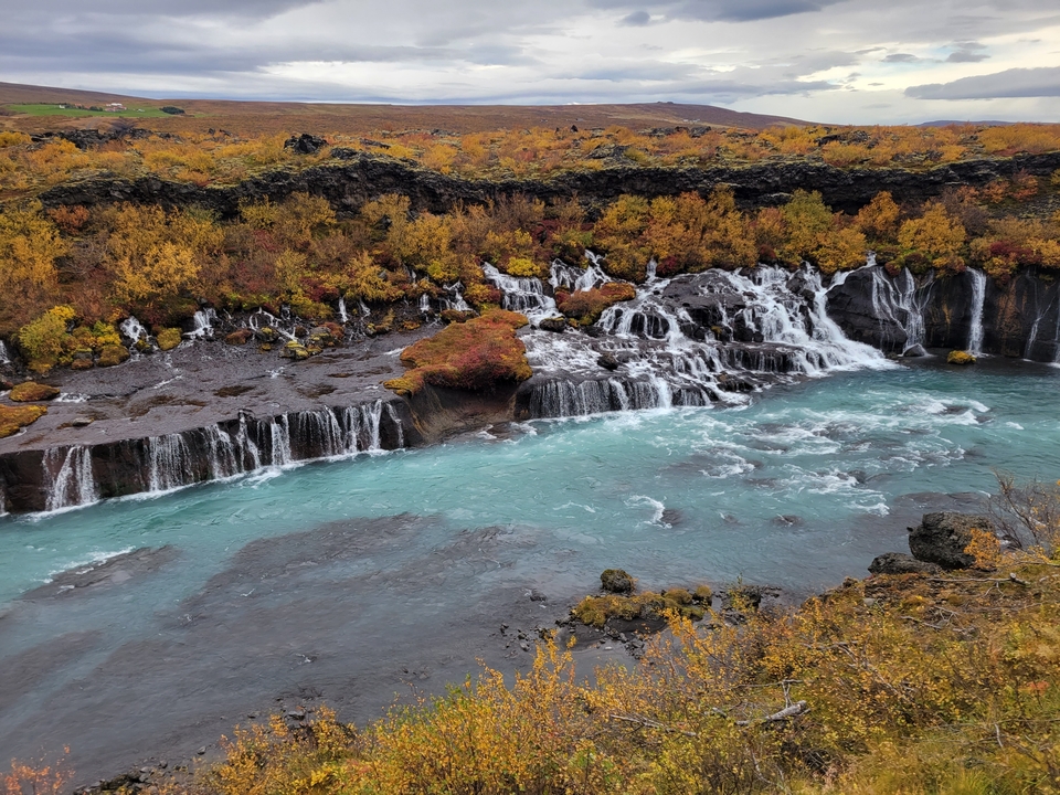 Waterfalls cascading into a turquoise river surrounded by fall foliage.