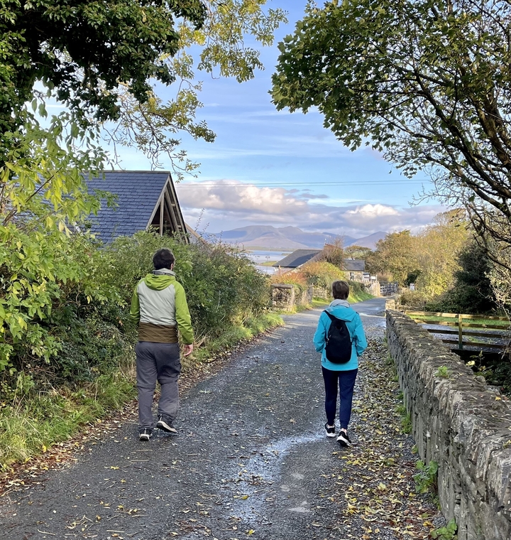 Couple walking down a rural path with mountains in the background.