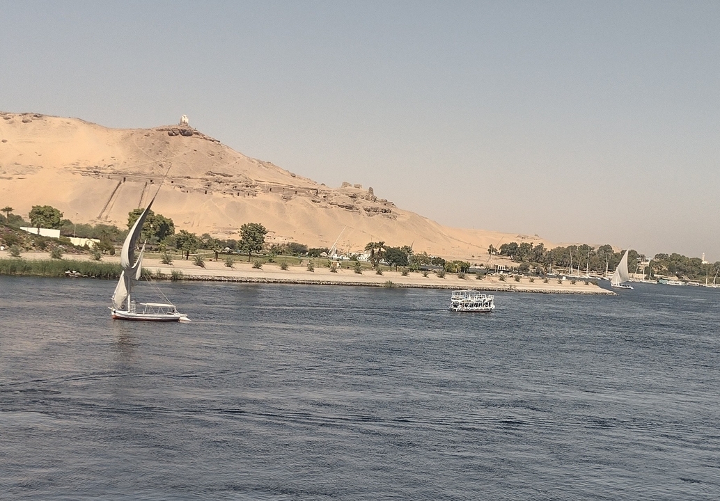 Sailboats on a river with a desert backdrop.
