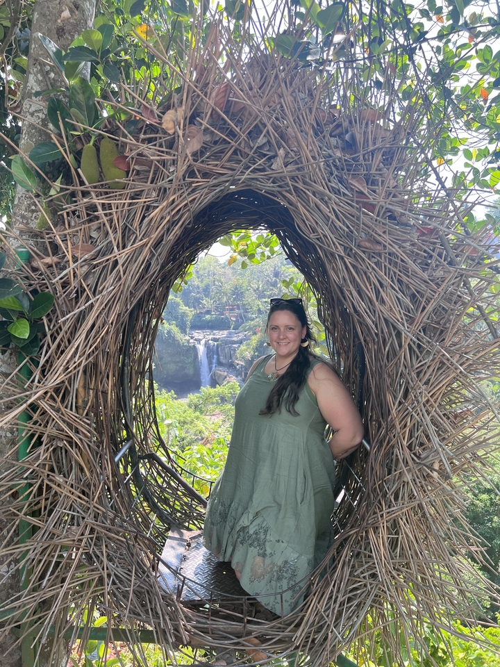 Woman posing in a woven nest with scenic waterfall behind.