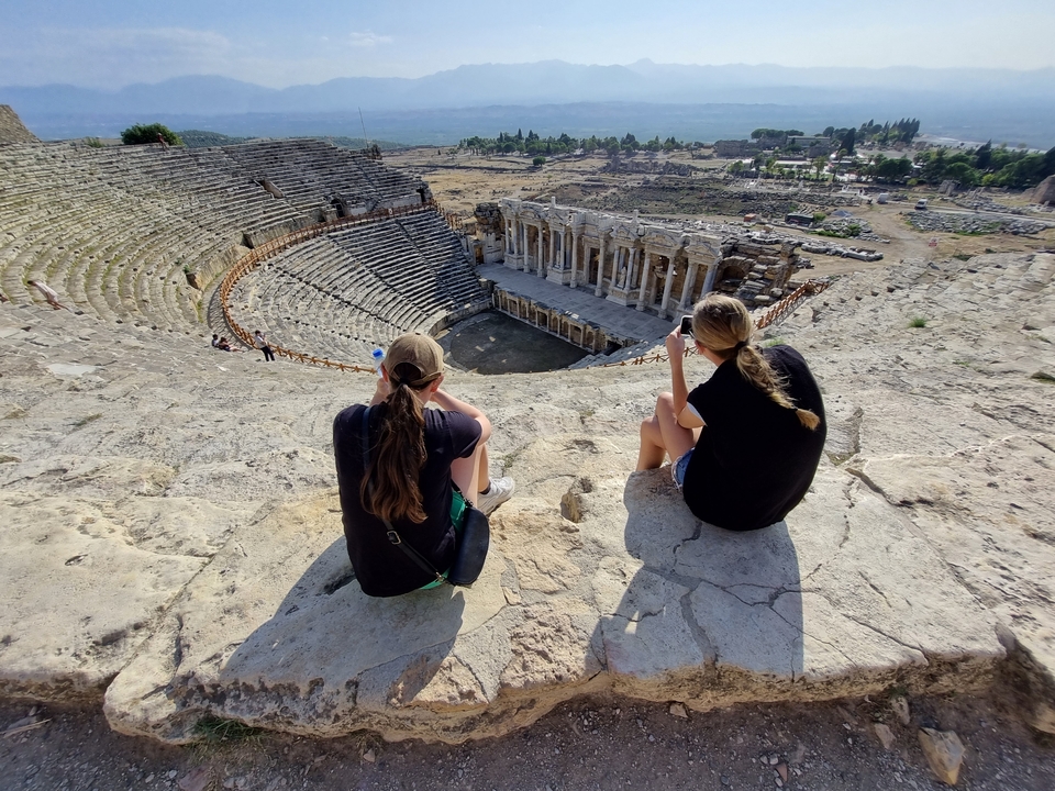 Two people sitting on ancient amphitheater steps admiring the view.