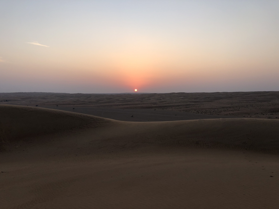 Desert landscape at sunset with the sun on the horizon.