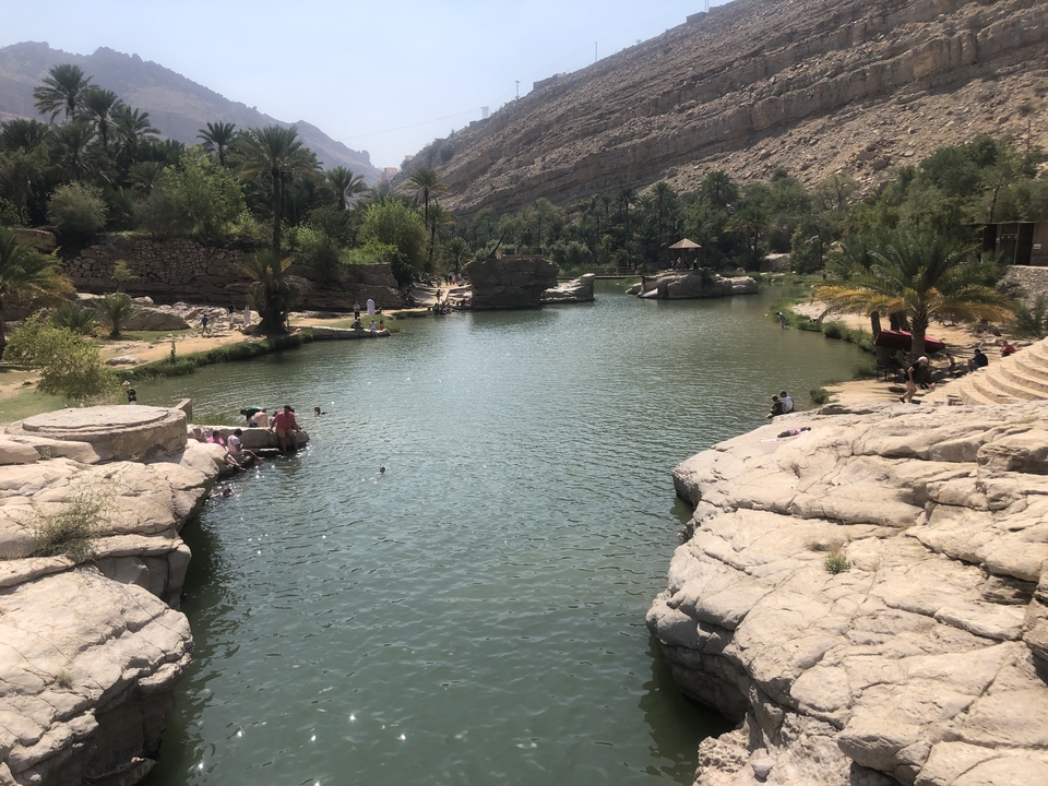 People swimming in a natural pool surrounded by rocky cliffs and vegetation.
