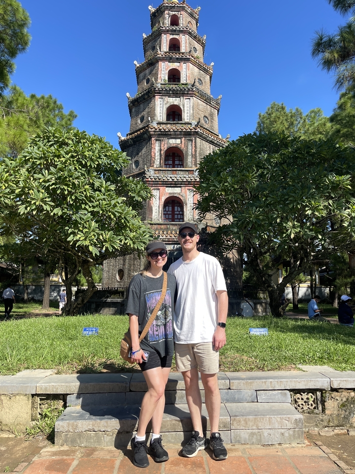 Deux personnes posant devant une pagode entourée d'arbres.