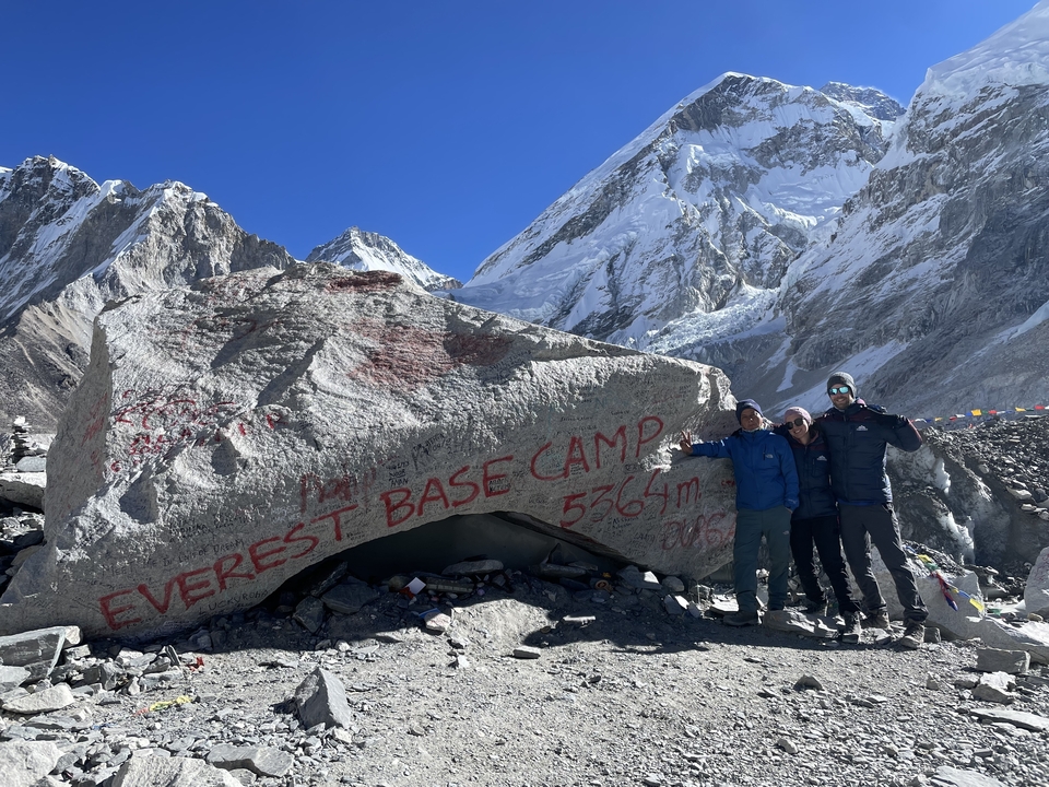 Three people posing in front of a rock with Everest Base Camp written on it.