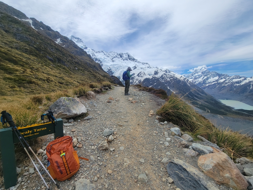 Personne marchant sur un sentier de montagne avec des sommets enneigés.
