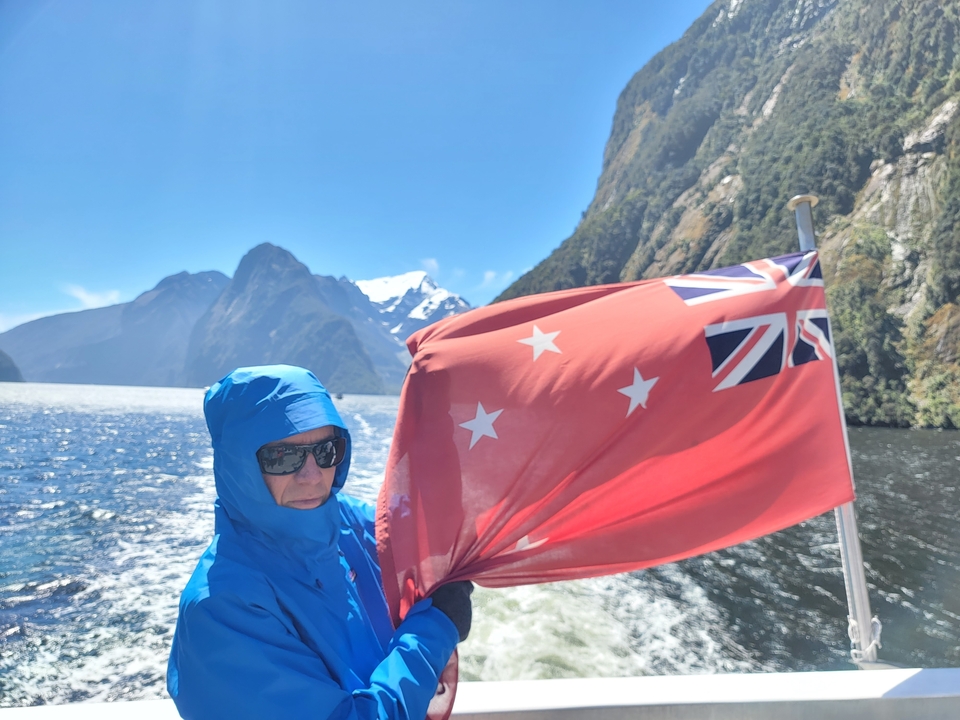 Une personne tenant un drapeau sur un bateau avec des montagnes en arrière-plan.