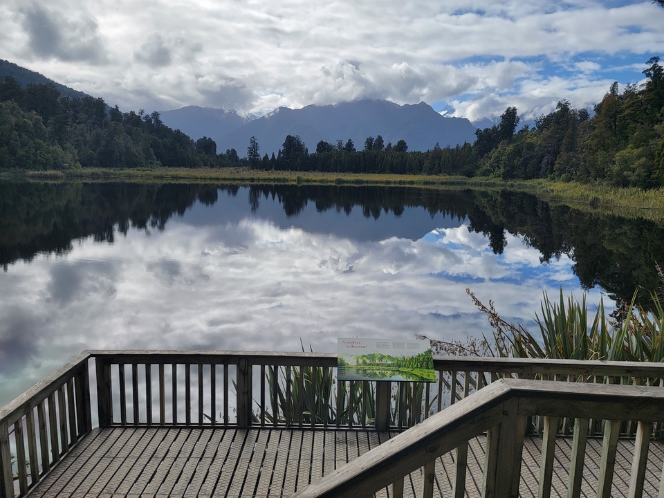 Reflet de montagnes dans un lac avec une plateforme d'observation.