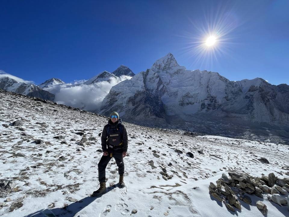 Hiker standing on a snowy terrain with majestic mountains under a deep blue sky.