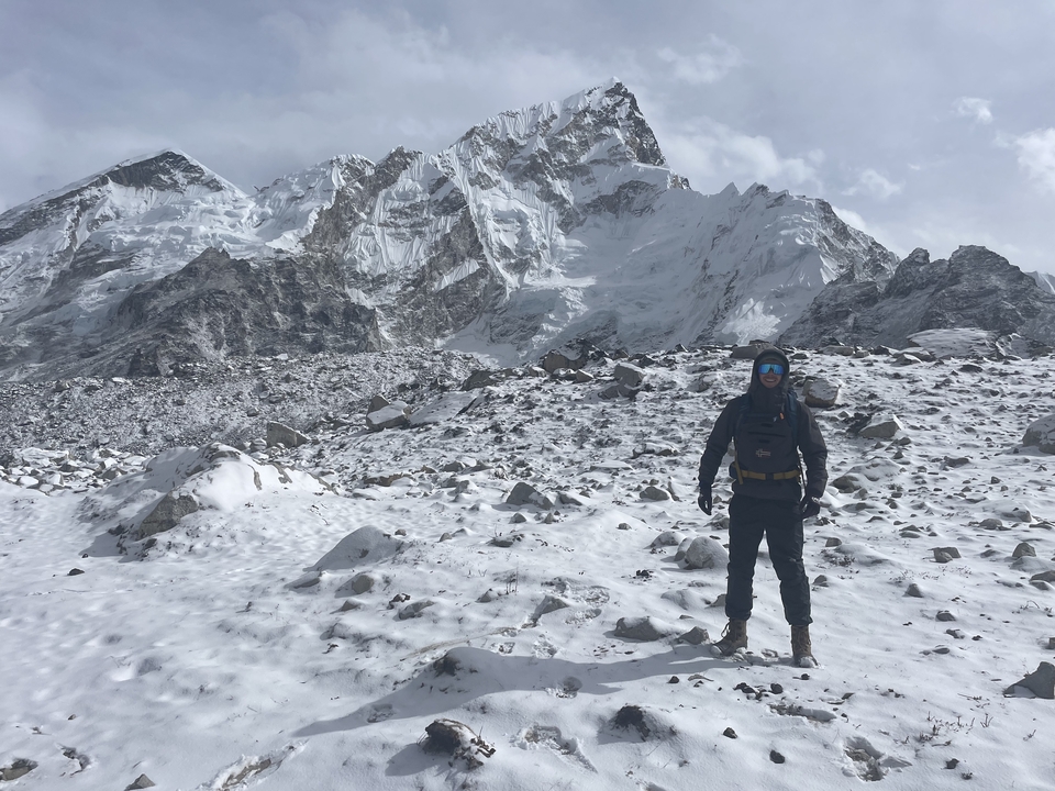 Explorer standing on snowy summit with jagged peaks in the distance.