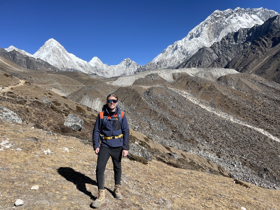 A person hiking in a vast mountainous area with dry terrain and clear skies.