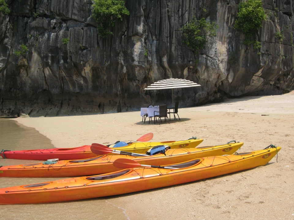 Des kayaks sur une plage avec une table dressée sous un parasol et des falaises en arrière-plan.