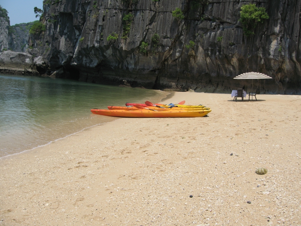 Kayaks colorés sur une plage de sable près d'une eau calme.