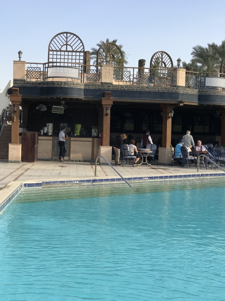 Au bord de la piscine avec des tables, des chaises et des gens qui se détendent.