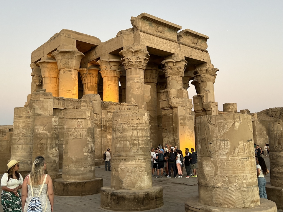 Ruines de temple avec des colonnes illuminées la nuit et des gens autour.