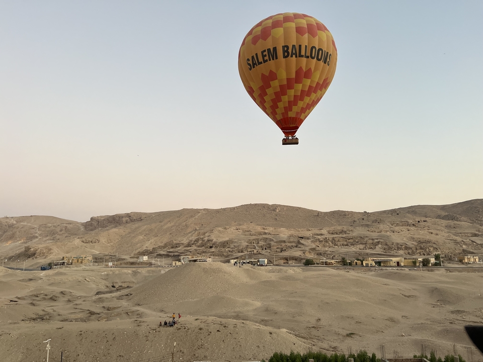 Montgolfière survolant un paysage désertique au lever du soleil.
