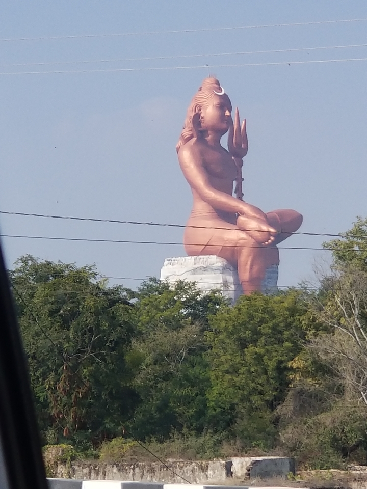 Groot standbeeld van een zittende figuur te midden van bomen.