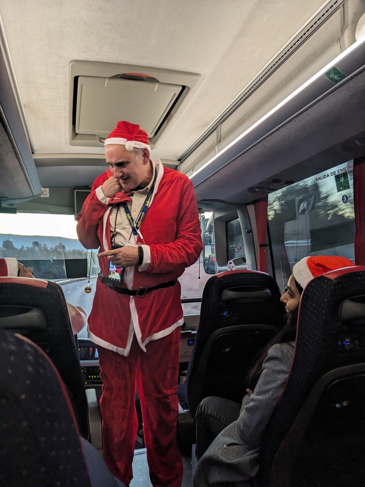 Man dressed in a Santa outfit talking on a bus.
