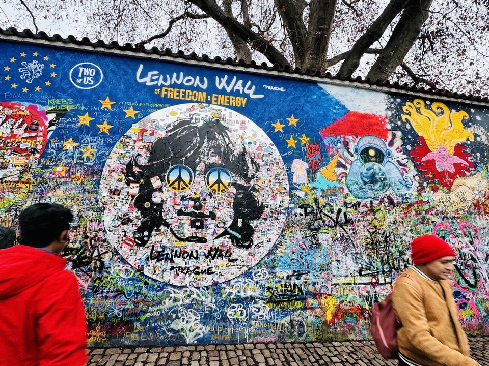 A vibrant graffiti wall depicting Lennon with tourists nearby.