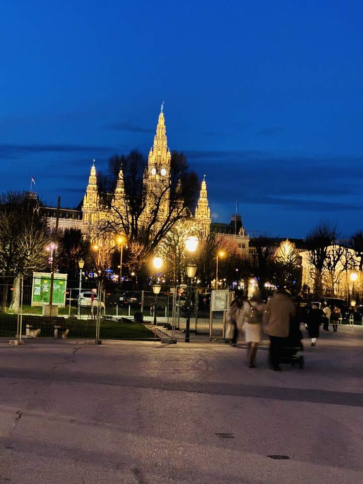 A night scene of an illuminated building with people walking in the foreground.